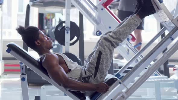 Muscular African Fitness Man Exercising on Leg Press Machine at the Gym
