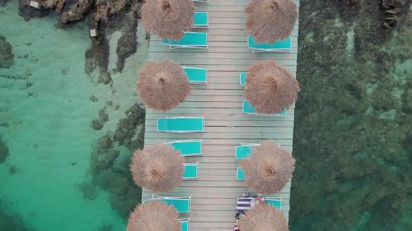 Aerial View of Empty Sunbeds Under Thatched Umbrellas on a Pier in Turquoise Sea