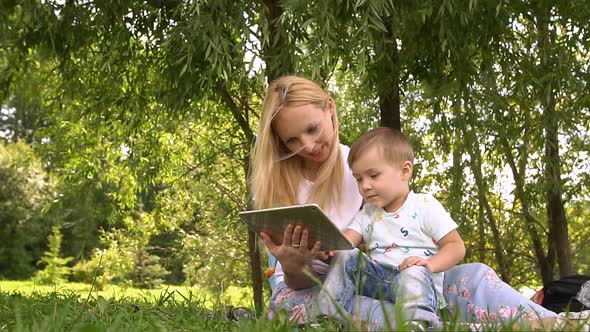 Happy Mother and Her Little Son Enjoying Playing on Tablet Computer in the Park. Slow Motion.