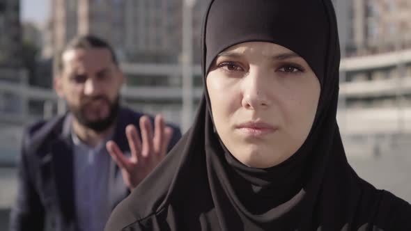 Close-up Face of Beautiful Muslim Woman with Sore Eyes Looking at Camera As Blurred Man Gesturing