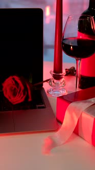 Online Date Concept Red Candles Bottle of Wine and Present Gift in Front of Laptop