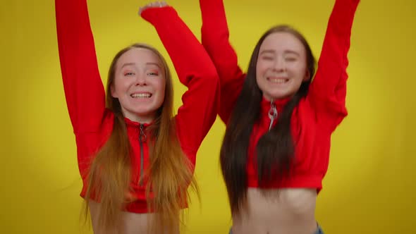 Excited Twin Women Gesturing Victory Jumping at Yellow Background Smiling