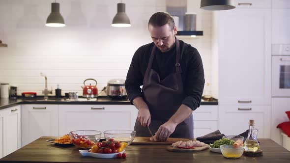 Young Cute Chef Cuts Chicken Meat on a Wooden Board at the Home Kitchen