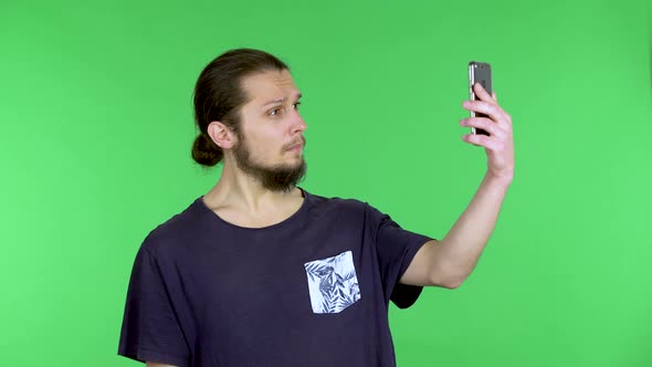 A Man Takes a Selfie on His Smartphone Smiles at the Camera and Makes a Victory Gesture Then Looks