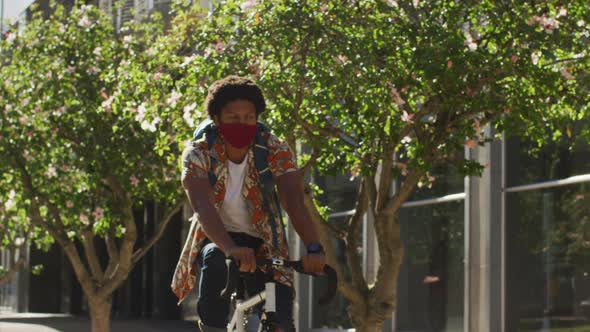African american man in city, wearing face mask riding bicycle in street