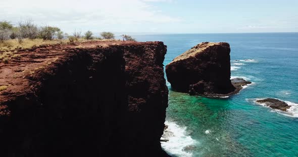 Drone sitting at a stationary level while man runs to the cliff peak.