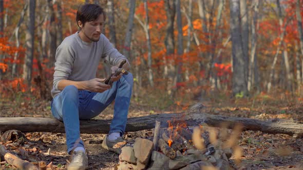 Young Man Sitting By a Bonfire in a Cold Autumn Forest. Autumn Vacation Concept