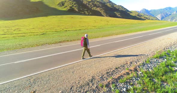 Flight Over Hitchhiker Tourist Walking on Asphalt Road. Huge Rural Valley at Summer Day. Backpack