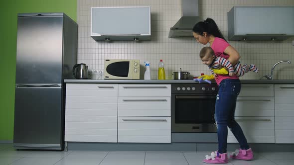 Mother Holding Baby and Cleaning Kitchen Surfaces