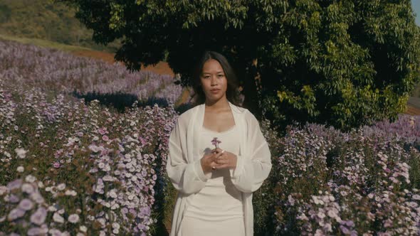 Young Asian Woman in Flower Field on Sunset Look at Camera