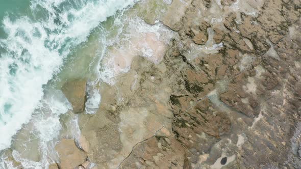 Dramatic Aerial Scene with Green Ocean Waves Crashing on Brown Rocks with White Foam and Splashes