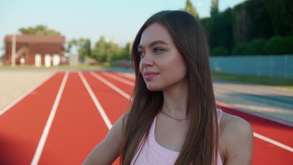 Confident Young Dark Blond Female Fitness Guru Standing on Red Sports Track with Arms Crossed and