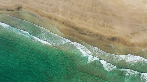 Fly over Kvalvika beach with splashing sea waves