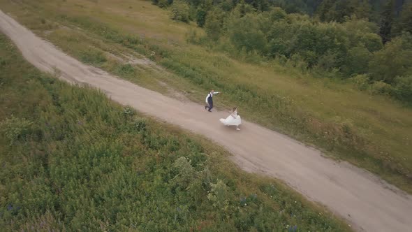 The Groom Runs with Bride on a Mountain Hills. Aerial Drone Shot
