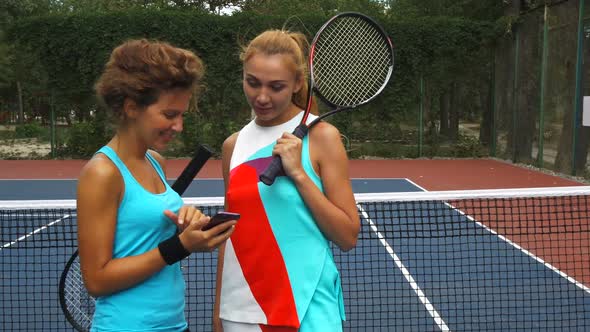 Two Tennis Girls Discussing While Sharing a Smartphone