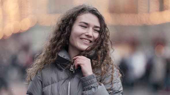 Portrait of a Young Smiling Woman with Curly Hair Dancing on a City Street Wearing a Jacket Cold