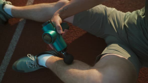 An Athlete Massages with a Percussion Therapy Gun to Relieve the Pain of Muscle Aches After a