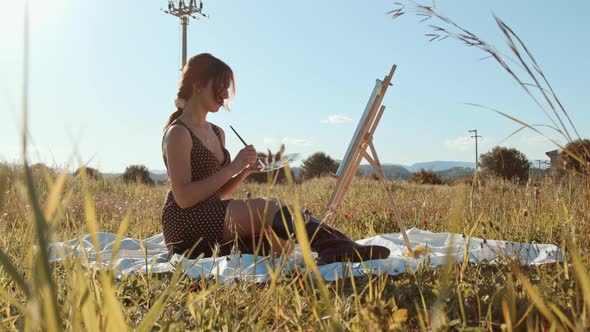 Young girl paints a picture sitting on the grass