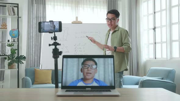 Teacher With Glasses Shoots Video By Smartphone While Having Video Call On Laptop And Teaching Math