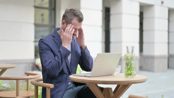 Man with Headache Working on Laptop Sitting in Outdoor Cafe