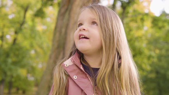 Cute Little Caucasian Girl Looks Up at Her Mom and Talks with a Smile in a Park  Closeup