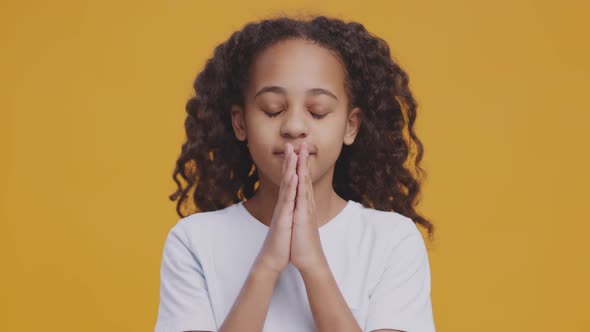 Concentrated Teen Black Girl Praying to God Over Orange Studio Background Making Cherished Wish