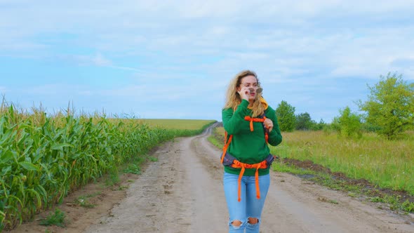 A Woman Goes Along a Cornfield on a Dirt Road