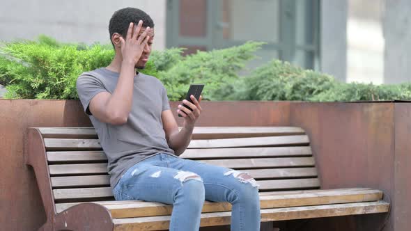 Upset Young African Man Having Loss on Smartphone on Bench 