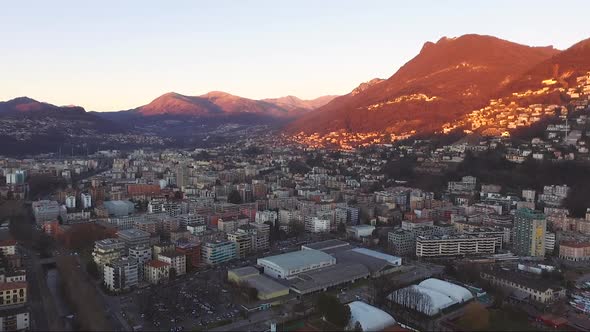 Aerial view of a beautiful city surrounded by mountains, next to a lake, during a sunset in autumn.