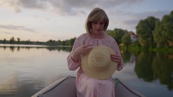 Cheerful Relaxed Caucasian Adult Trans Woman in Pink Romantic Dress Holding Straw Hat in Hands and