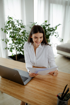 Woman holding paper, doing paperwork, reading good news, checking post mail sitting at home table. / Photodune, Misc