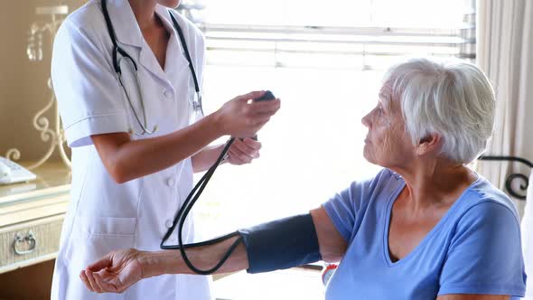 Female doctor checking the blood pressure of senior woman in the bedroom