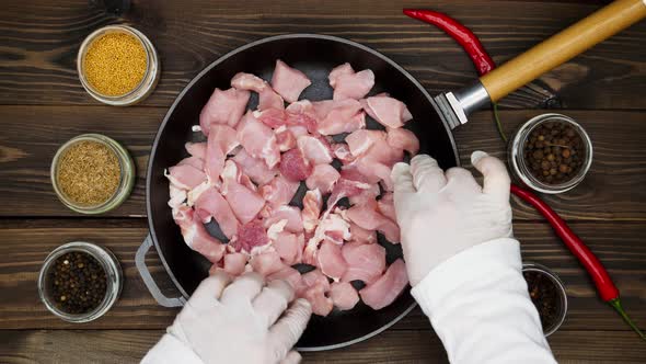 The cook puts the meat on the pan. Diced pork in a cast iron skillet. A metal frying pan