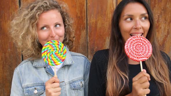 Two Young Mixed-Race Girls Licking Lollipops Smiling At Camera