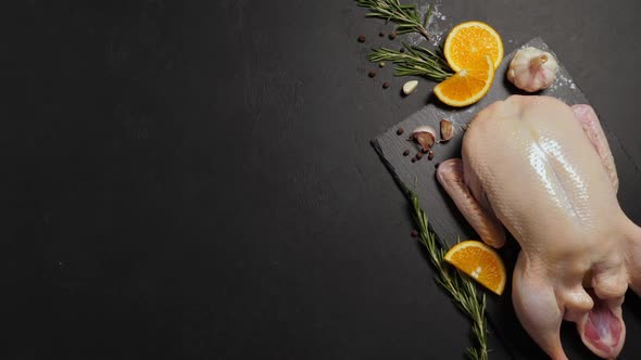 Raw Organic Whole Duck with Cut Orange and Rosemary on Slate Board on Black Background