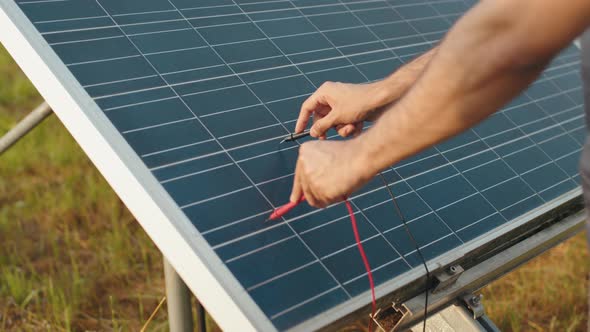 Close Up of Male Hands Checking Voltage in Solar Panels with Multimeter Outdoors