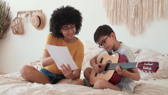 Woman Teacher Teaches Child to Play Acoustic Guitar Using Notes