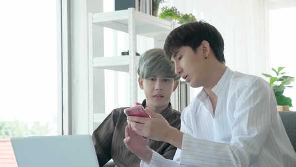 Asian gay couple using laptop and smartphone, discussing somthing seriously