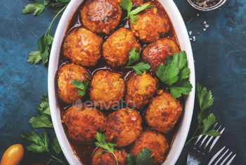 Meatballs with spicy tomato sauce in white baking dish on blue kitchen table. Top View / Photodune, Misc