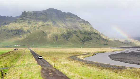 Aerial of a Car Driving on a Mud Dirt Road Between Green Fields in Iceland