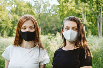 Two red-haired and brown-haired girlfriends in black and white face mask on nature background / Photodune, Misc