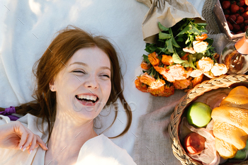 Top view candid portrait of young red-haired woman lying on a picnic blanket near flowers and basket / Photodune, Misc