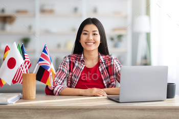  Sitting At Table With International Flags And Laptop Computer, Young Korean Female Student Enjoying Distance Learning And Remote Education