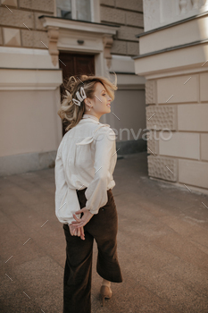 Happy blonde curly woman in brown velvet pants and white blouse walks outdoors. Charming lady smile / Photodune, Misc