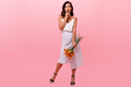 Girl looks at camera in surprise and holds orange flowers. Cute surprised woman in long light skirt - PhotoDune Item for Sale