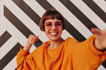 Cheerful short-haired girl in bright clothes smiling outside. Modern woman in sunglasses making sel / Photodune, Misc