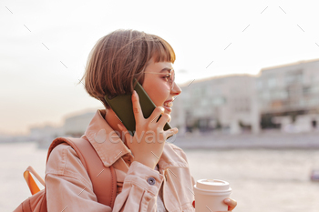 Short-haired woman talking on phone outside. Optimistic girl in sunglasses and beige denim jacket h / Photodune, Misc
