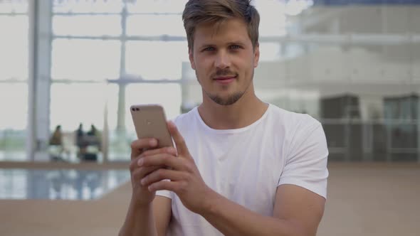 Smiling Young Man Holding Smartphone and Looking at Camera