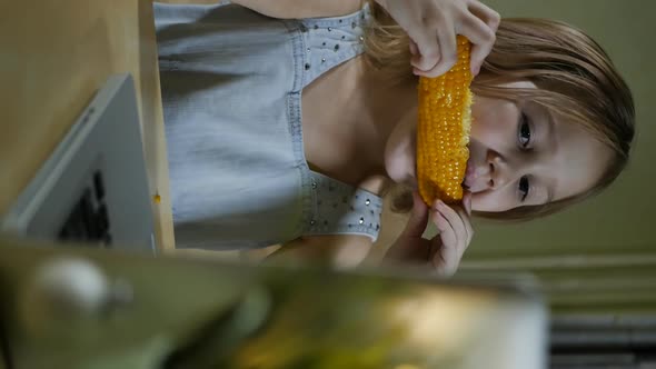Vertical Screen Girl Eating Boiled Sweet Corn and Looking at Laptop