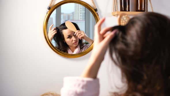 Woman Brushing Hair in Front of Bathtub Mirror